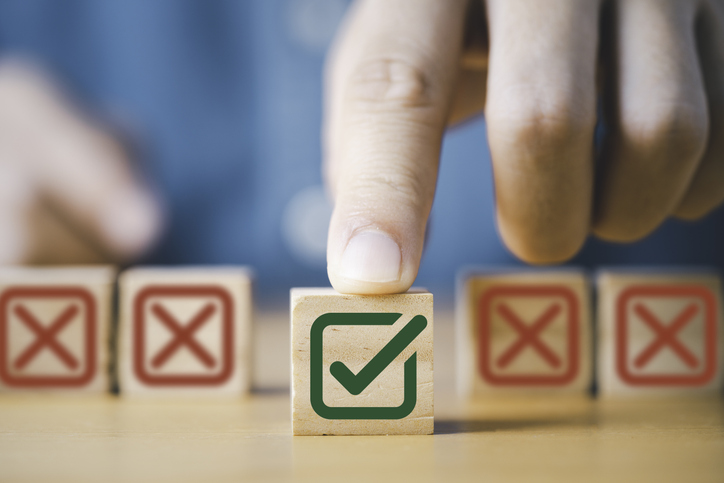 Hand pushing green correct sign symbol in front of Red Cross sign on wooden block cubes