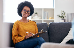 Substance abuse counselor on sofa, writing notes and listening to patient.