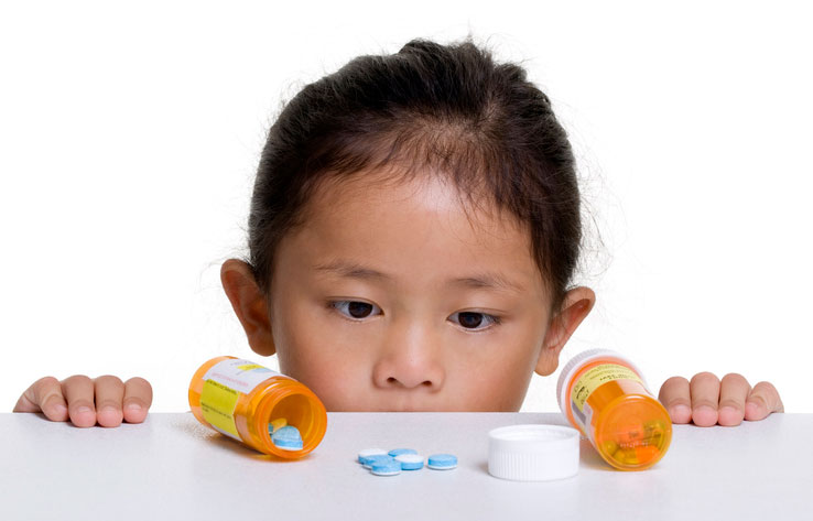 young girl looking at pill bottle and pills on table