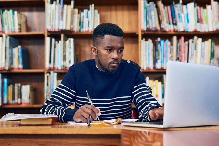 young man in library doing online school work